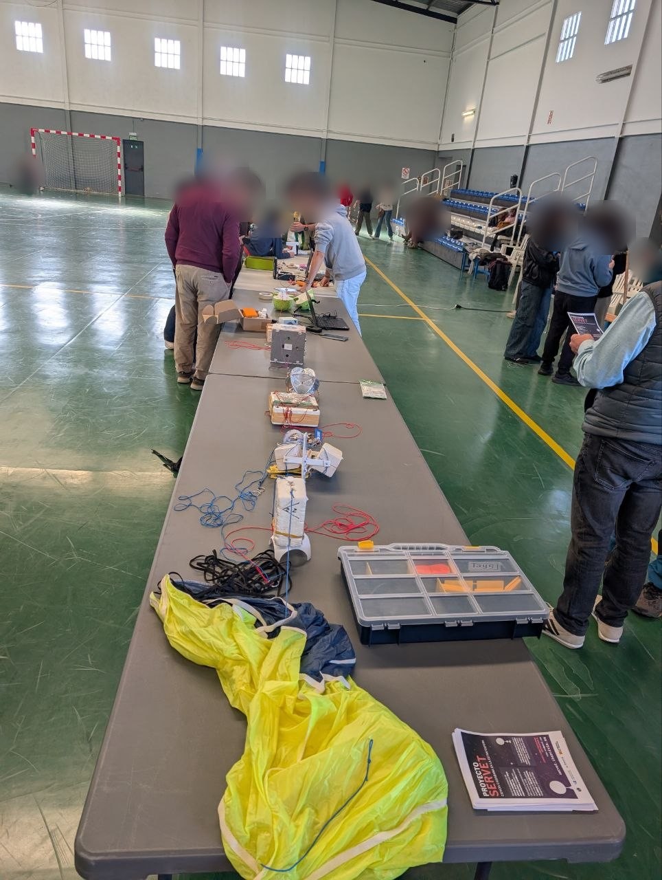 Table with the Servet XII capsules lined up next to the yellow parachute, with participants in the background