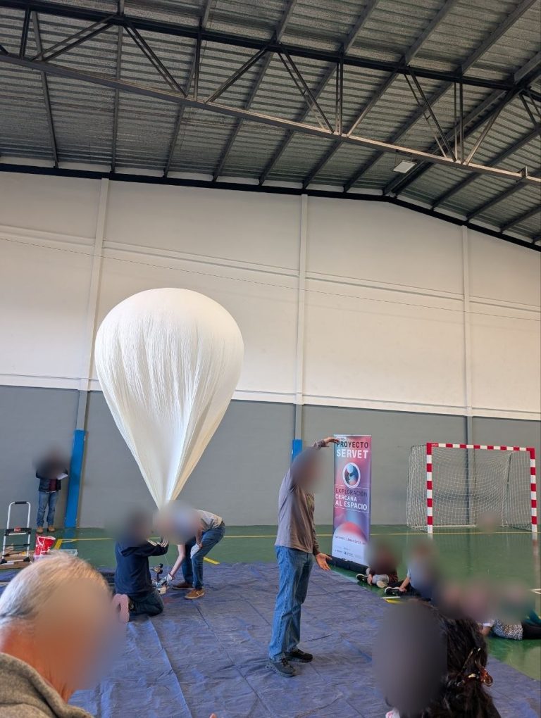 Participants inflating the helium balloon in the Lumpiaque sports hall, with children sitting and watching
