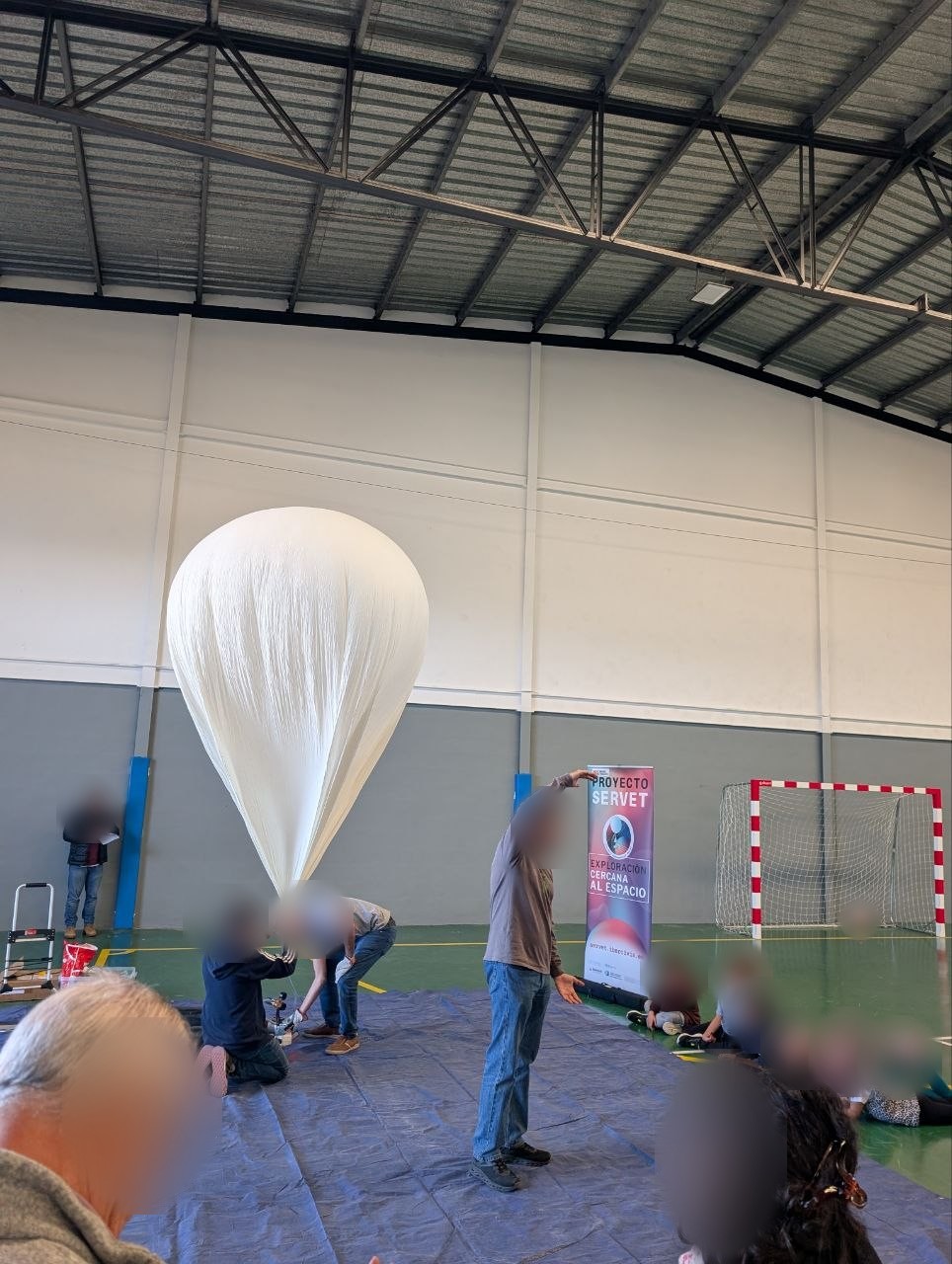 Participants inflating the helium balloon in the Lumpiaque sports hall, with children sitting and watching